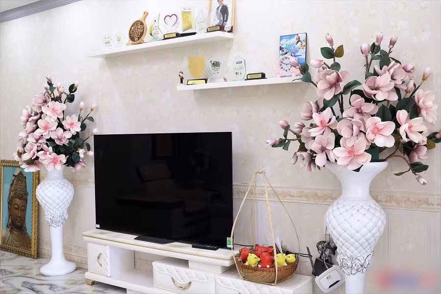 Trắng là tông màu chủ đạo trong ngôi nhà của Lê Dương Bảo Lâm. 27 Tết vừa rồi, vợ chồng nam diễn viên mới dọn về ở nên căn nhà vẫn đang trong giai đoạn sắm sửa, hoàn thiện dần dần. Kệ tivi với hai chậu hoa giả lớn hai bên được tự tay vợ nam diễn viên kết và bày trí ở giữa phòng khách.