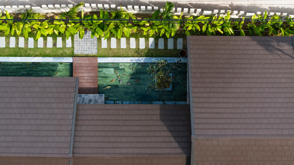 Thay vì lối vào trực tiếp, lối vào nhà đi qua một hành lang xanh tươi và con đường bằng đá tự nhiên được trang trí bằng cây xanh tươi mát và hồ cá Koi, mang đến bầu không khí trong lành.