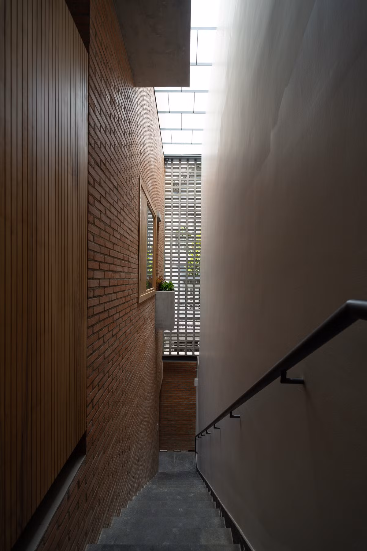 Mảng tường này dẫn dắt cầu thang từ trệt lên lầu như một cầu thang ngoài trời và tạo ra ranh giới giữa ngôi nhà với khoảng hẻm nhỏ bên hông nhà. Ảnh: Quang Dam/G+architects