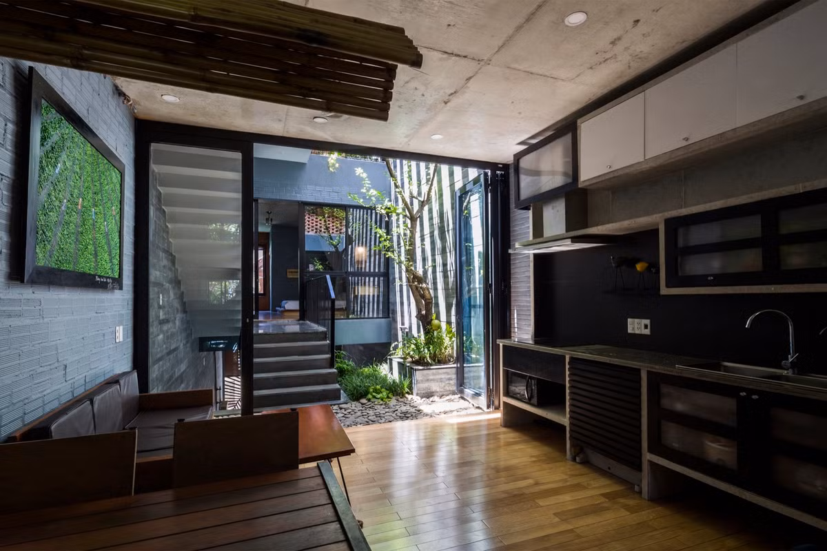 Phòng bếp và phòng khách đặt tại tầng 2, tiếp giáp với bồn cây. Phòng chung thiết kế thô mộc với trần đổ bê tông, tường gạch xây thô.