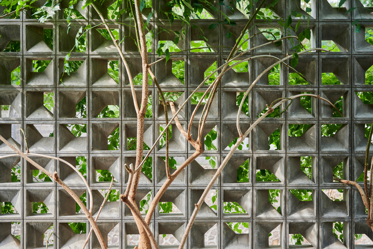 Mái nhà tạo một góc dốc hình khung chữ A kết hợp khoảng đệm tại mặt tiền bằng gạch hoa gió giúp thông gió thụ động.