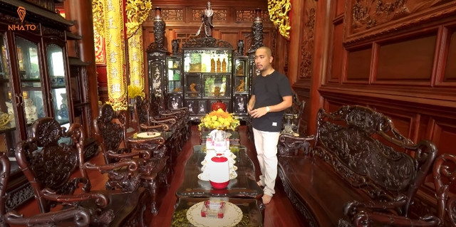 Không gian nhà chính nổi bật với phần tường và trần đều ốp gỗ 100%, đi kèm các món nội thất hoài cổ như bộ tràng kỷ làm bằng gỗ trắc, tủ gỗ khảm trai.... Ảnh chụp màn hình NhaTo