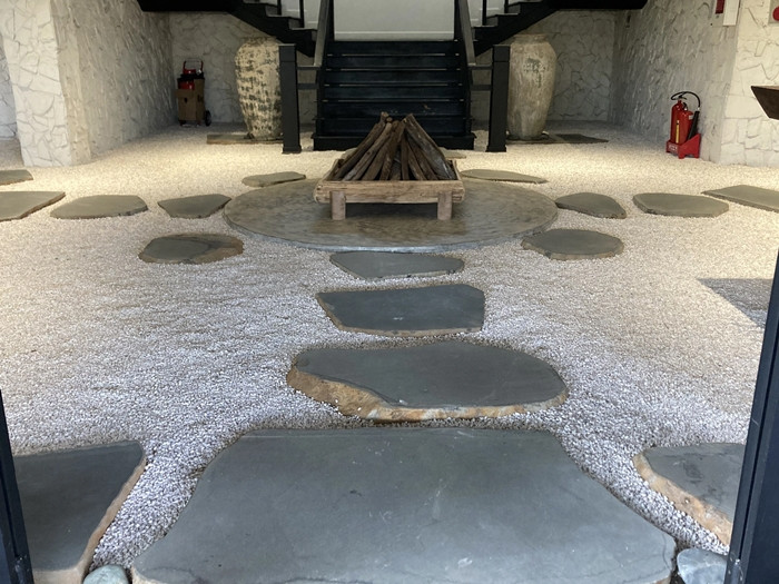 Nền nhà được rải đá dăm trắng, lối đi là những phiến đá lớn, màu sẫm nổi bật. Chính giữa sảnh tầng trệt đặt một khối hình vuông, bên trong là củi khô gác lên nhau, giống như bếp lửa. Ảnh: Dân trí