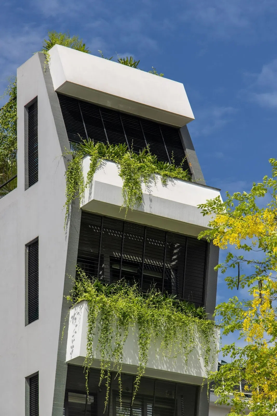 Để đối phó với ánh nắng gay gắt chiếu thẳng vào mặt tiền hướng Tây Nam, kiến trúc sư thiết kế hệ thống bồn hoa và ban công đua ra ở các tầng, tạo nên "tòa lâu đài xanh" giữa lòng đô thị. Ảnh: Hoàng Lê - Kiến Trúc NDT