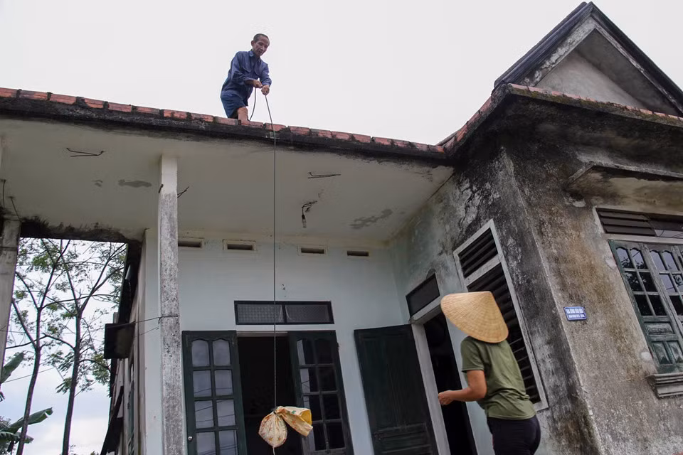 Từ sáng sớm nhiều hộ gia đình đã lấy đất, cát đổ vào bao tải, mang lên mái nhà, mái tôn chằng chéo tránh bị tốc mái. Bà Nguyễn Thị Quế (51 tuổi) trú xã Cẩm Thăng, huyện Cẩm Xuyên (Hà Tĩnh) cho biết gia đình còn hai ông bà, nghe đài báo bão, từ sáng hai vợ chồng phải dùng cát bỏ vào bao bì mang lên đặt trên mái nhà, tránh bị tốc mái khi bão vào. “Năm nào cũng thế, nghe bão là gia đình tôi lại mang cát, đất bỏ vào bao đặt khắp mái nhà”, bà Quế nói. Ảnh: Phạm Trường.