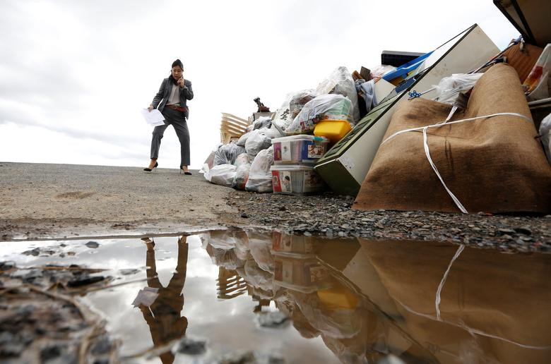 Người phụ nữ đứng nói chuyện qua điện thoại gần đống rác ngổn ngang ở Koriyama ngày 15/10. Được biết, Nhật Bản đã phải huy động hàng trăm nghìn thành viên của lực lượng cứu hộ, cảnh sát, quân đội,...để tham gia vào hoạt động cứu trợ người dân sau bão.