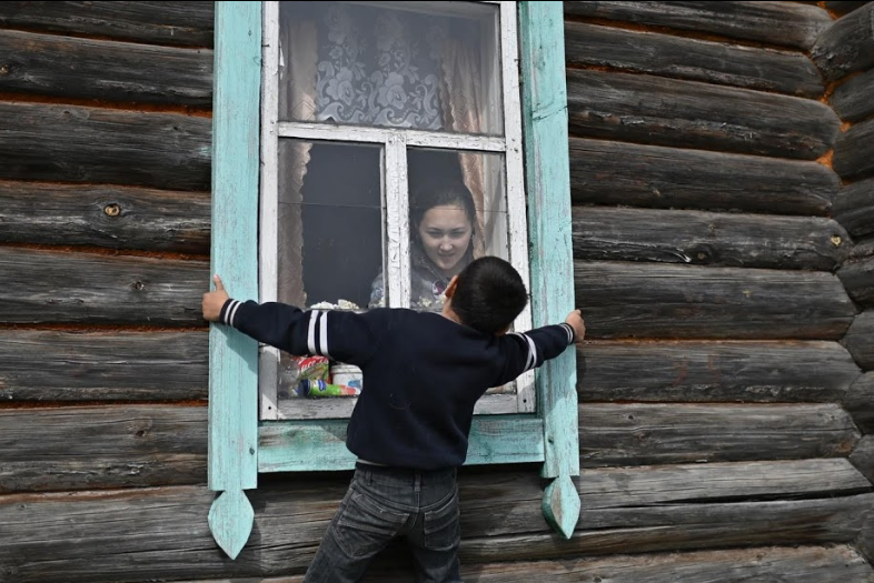 Ravil nói chuyện với chị gái, Rozalia, qua cửa sổ. Ngôi nhà của Ravil được xây bằng những cây gỗ chắc chắn.