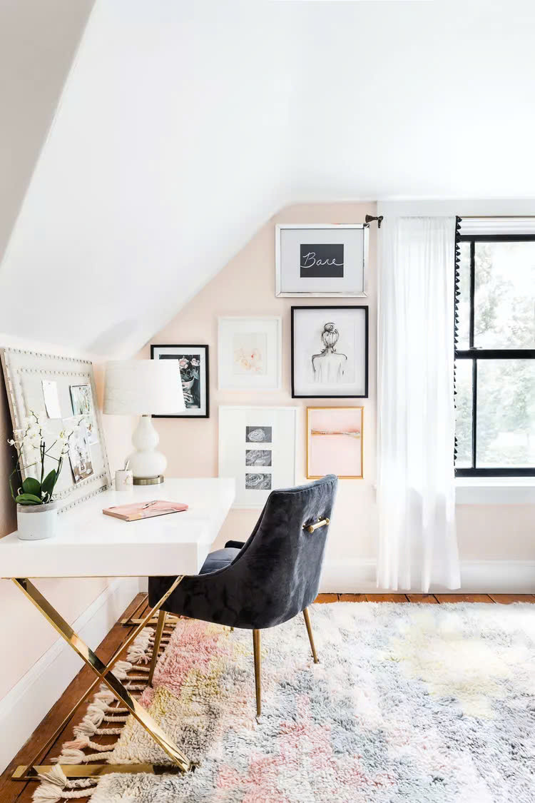 Không gian học tập trong phòng ngủ với tường màu hồng, bàn màu trắng và ghế màu đen. Tranh nghệ thuật đóng khung và bảng thông báo bọc nệm không chỉ dùng để ngắm khi cần thư giản mà còn có thể đóng vai trò như một động lực thúc đẩy.