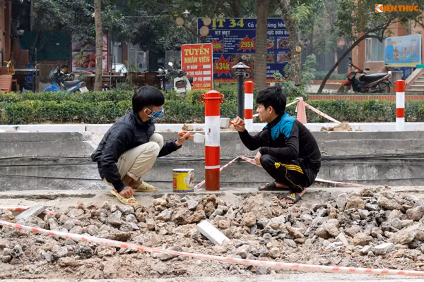 Hai công nhân nhanh tay phủ lớp sơn mới lên cọc tiêu dọc tuyến đường.