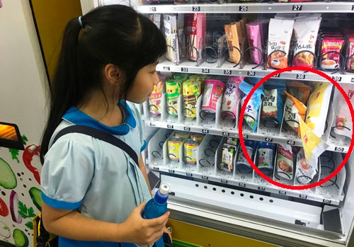 Khách hàng là bé gái "chưng hửng" khi gói xoài sấy bị sự cố kẹt lại trên kệ hàng.