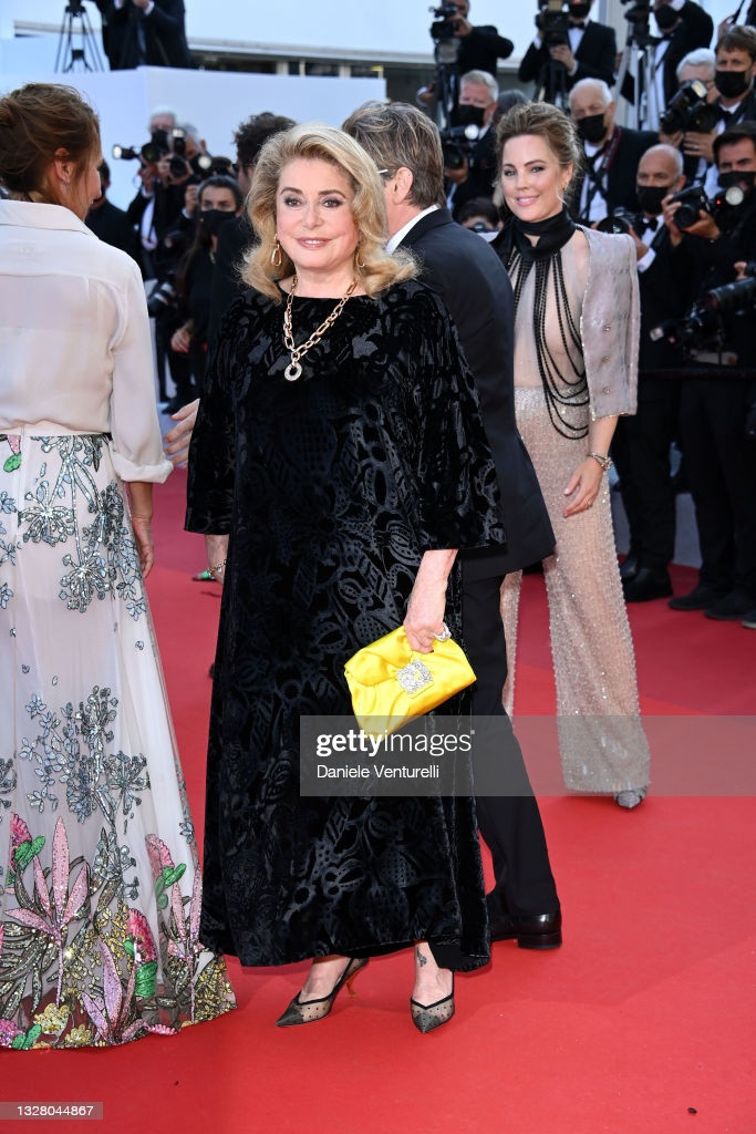 Ngôi sao gạo cội Catherine Deneuve đến dự thảm đỏ với thiết kế nhung đen, họa tiết in chìm, ánh kim sang trọng. Minh tinh người Pháp biết cách chọn trang phục phù hợp với lứa tuổi, kèm theo đó là kiểu trang điểm nhẹ nhàng để không bị "làm lố" trên thảm đỏ. Chi tiết vòng cổ lớn và clutch màu vàng nổi bật là điểm nhấn trang phục của huyền thoại điện ảnh người Pháp.