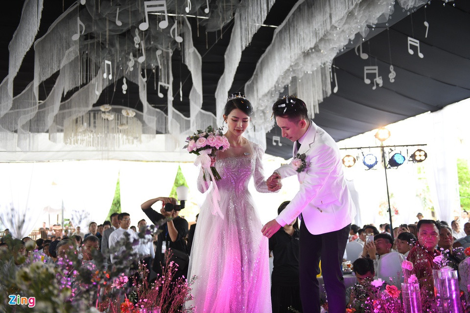 Chú rể Mạnh Quỳnh và cô dâu Khánh Vy tiến vào lễ đường trong tiếng vỗ tay của quan khách. Khoảng 700 khách mời là bà con, hàng xóm tại quê nhà đã đến tham dự và chúc phúc trong ngày trọng đại của cặp đôi. Toàn bộ ghế ngồi của khách đều được trang trí theo tông màu trắng.