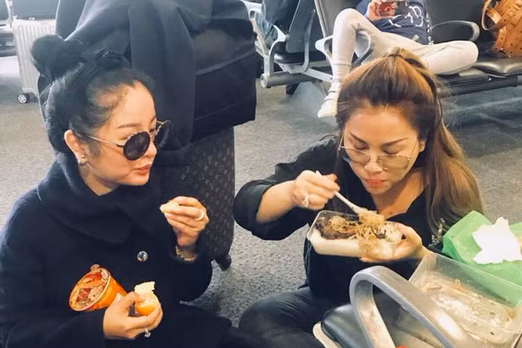 Tại sân bay, Minh Tuyết và Thúy Nga ngồi ăn mì gói, cơm hộp để lót dạ.