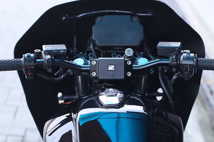 Ghi đông được hạ thấp ngang bằng với bình xăng và thẳng mang phong cách tracker, gắn trên nó là bọc tay lái Biltwell và cụm công tắc mới. Đầu đèn hình chữ nhật đặc trưng của dòng CBX cảnh sát được bố trí lại.