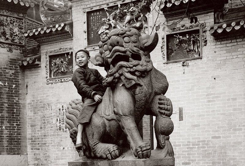 Một cậu bé tinh nghịch cưỡi trên lưng sư tử đá.