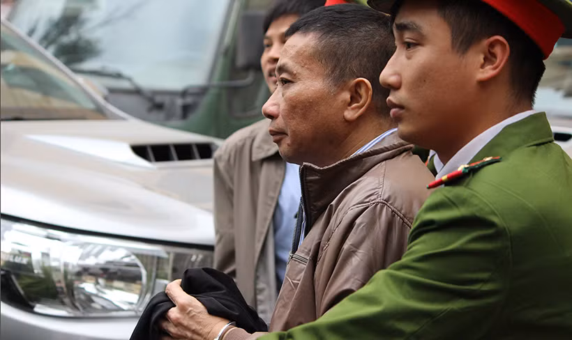 Bị cáo Ninh Văn Quỳnh, nguyên Trưởng ban Tài chính kế toán và Kiểm toán PVN lĩnh 7 năm tù, được cảnh sát dùng áo phủ tay che còng số 8 khi dẫn giải ra xe thùng đưa về trại giam.