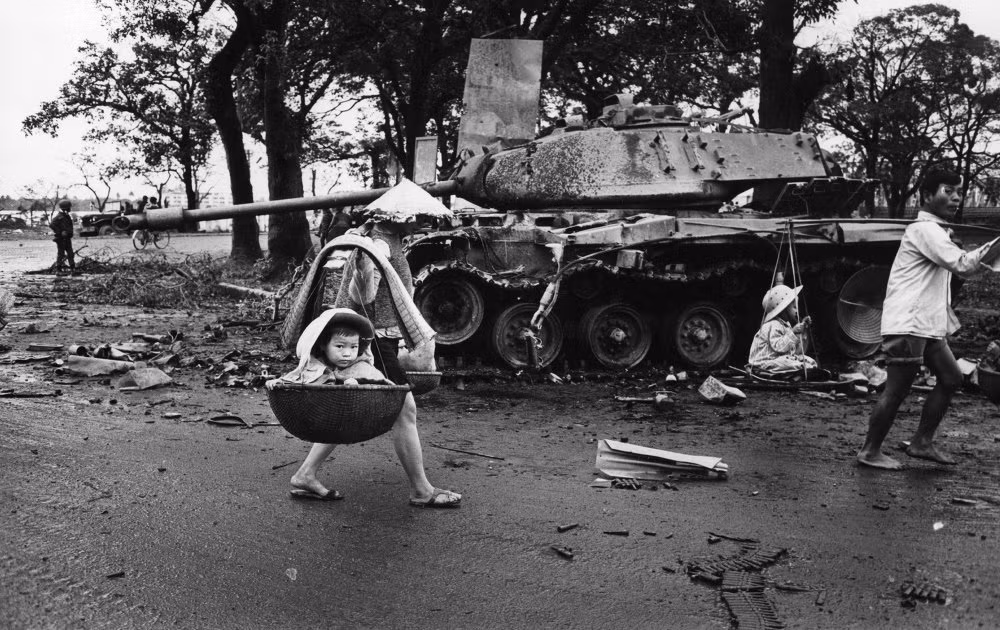 Theo ước tính, số lượng người Việt Nam thiệt mạng trong cuộc chiến tranh khốc liệt đó rơi vào khoảng 800.000 - 3,1 triệu người. Trong ảnh là người mẹ dùng đòn gánh đưa con đi trú ẩn.