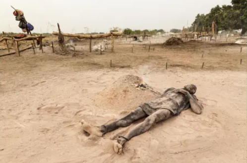 Một người đàn ông trong bộ lạc nằm cách đống lửa được đốt từ phân bò không xa. Bộ lạc này dùng tro từ phân bò bôi lên da như một biện pháp chống nắng.