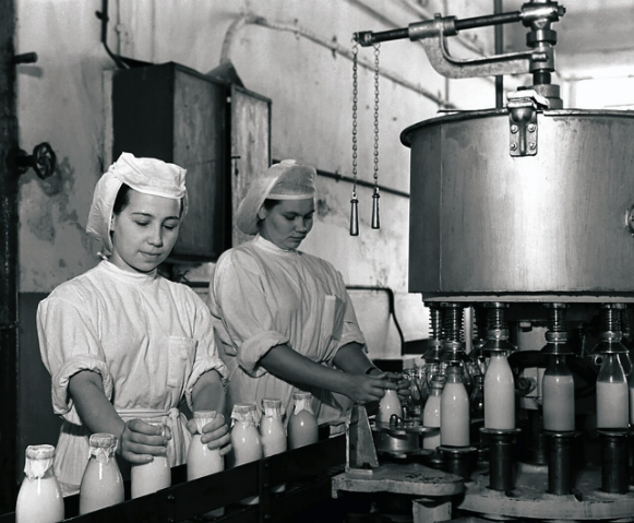 Bức ảnh này chụp hai người phụ nữ làm công việc đóng chai sữa trong nhà máy.