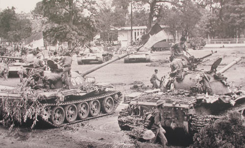 Tại triển lãm, người xem được nhìn lại những bức ảnh nổi tiếng của nghệ sĩ Đinh Quang Thành, trong đó có bức “Quân đoàn 3 truy kích địch trong sân bay Tân Sơn Nhất”. Nghệ sĩ Đinh Quang Thành vẫn bảo rằng, mình là người may mắn khi trực tiếp chứng kiến miền Nam được giải phóng. Nhờ đó mà ông lưu giữ được những khoảnh khắc ý nghĩa. Mặc dù không chụp được bức ảnh treo cờ trên nóc Dinh Thống nhất nhưng ông đã chớp được khoảnh khắc các chiến sĩ Sư đoàn 10, Quân đoàn 3 truy kích địch trong sân bay Tân Sơn Nhất. Đó cũng chính là tác phẩm ghi đậm dấu ấn trong phóng sự ảnh “Giải phóng Sài Gòn” của ông. Ảnh: Xe tăng số hiệu 390 húc đổ cổng Dinh Thống nhất cùng xe tăng 843 tiến vào án ngữ ngay trước thềm Dinh.