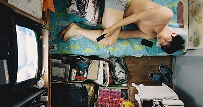 Một người đàn ông nằm trên một chiếc giường nhỏ gần như chỉ bằng cơ thể của mình trong phòng nhỏ.