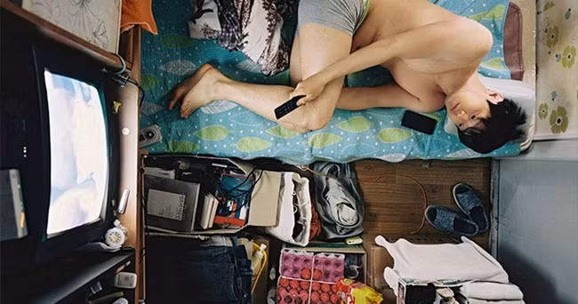 Một người đàn ông nằm trên một chiếc giường nhỏ gần như chỉ bằng cơ thể của mình trong phòng nhỏ.