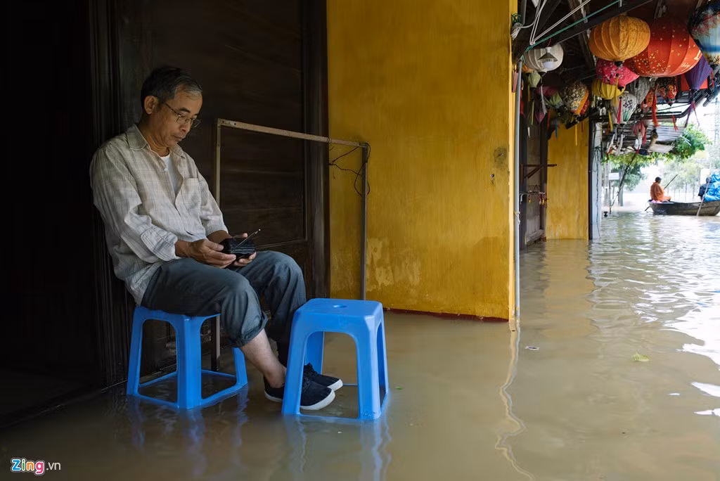 Do bị ngập từ trong ra ngoài, một người đàn ông ngồi dưới hiên nhà chờ nước rút.