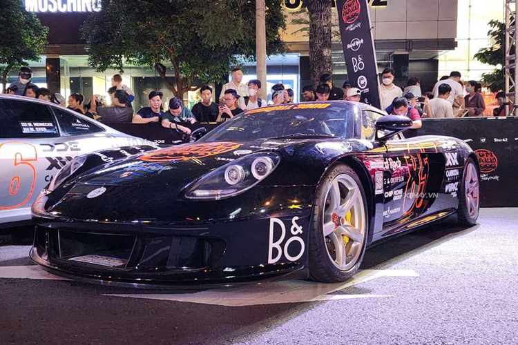 Chiếc Porsche Carrera GT đang góp mặt trong hành trình siêu xe lớn nhất thế giới mang ngoại thất màu đen với bộ tem chủ đạo màu cam nổi bật.