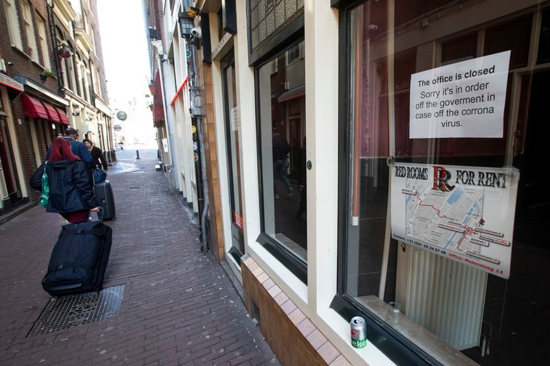 Du khách mang theo hành lý đi qua một khu phố đèn đỏ ở Amsterdam, Hà Lan, ngày 14/3. Ảnh: AP.