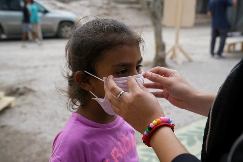 Andrea, một người xin tị nạn làm việc tại hiệu thuốc của khu trại tị nạn ở Matamoros, chỉ cho bé Perla, 7 tuổi, cách đeo khẩu trang đúng cách ngày 16/3.