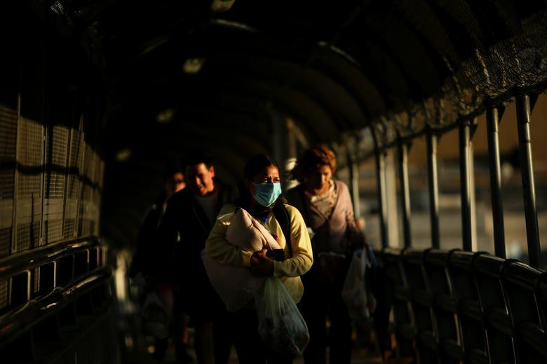 Người phụ nữ đeo khẩu trang bế con nhỏ khi đi bộ trên cây cầu biên giới quốc tế Paso del Norte về phía El Paso, bang Texas, ngày 13/3.