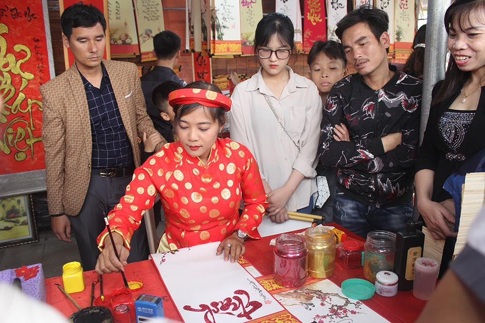 Ngoài lễ khai bút, chương trình còn có phần hội với nhiều hoạt động văn hóa, văn nghệ đặc sắc như chương trình giao lưu thơ, thi đấu các trò chơi dân gian (cờ tướng, kéo co, bắt chạch trong chum, nhảy bao bố…), thi đấu hót chim chào mào… Ảnh: Các học sinh chăm chú theo dõi "bà đồ" viết thư pháp.