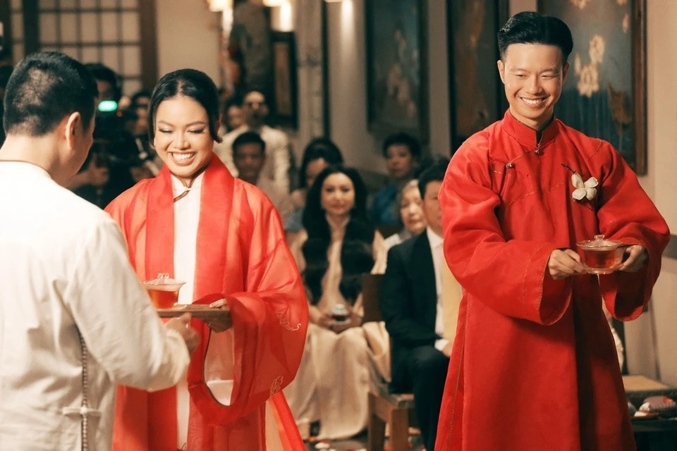 Đôi áo dài cưới có 5 tà mang ý nghĩa tượng trưng khác nhau. 2 tà trước đại diện cho cha mẹ, 2 tà sau là vợ chồng, tà thứ 5 ẩn phía bên trong biểu trưng cho con cái. 5 chiếc khuy xếp hàng dọc phía trước mang ý nghĩa của các đức tính đáng quý, bao gồm nhân, lễ, nghĩa, trí, tín. Áo của cô dâu được cách tân từ áo mệnh phủ của hoàng hậu thời xưa. Chiếc áo choàng chất liệu voan được bổ sung phía ngoài, gia tăng điểm nhấn. Hình ảnh chim hạc đại diện cho hạnh phúc vẹn tròn trong văn hoá Á Đông được thêu tay tỉ mỉ phía sau lưng.