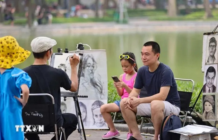 Đến với phố đi bộ Hồ Gươm, du khách trải nghiệm làm mẫu để có bức vẽ truyền thần làm kỷ niệm. (Ảnh: Thanh Tùng/TTXVN)