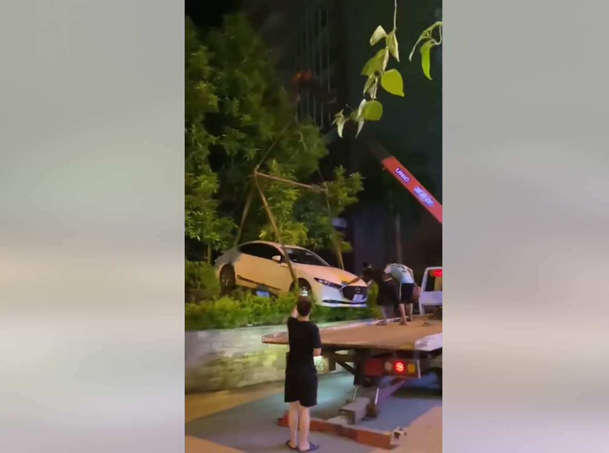 Người này cho biết, do chiếc xe ô tô Mazda 3 này đỗ xe không đúng quy định, chắn trước cửa nhà, chắn lối ra vào nên chủ nhà đã gọi xe cẩu đến nâng chiếc xe này giấu vào bụi cây. Ảnh: Cắt ra từ clip