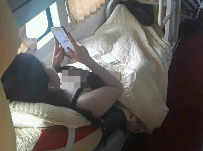 Một cô gái mặc áo hai dây vô tư nằm xem điện thoại trên xe khách giường nằm.