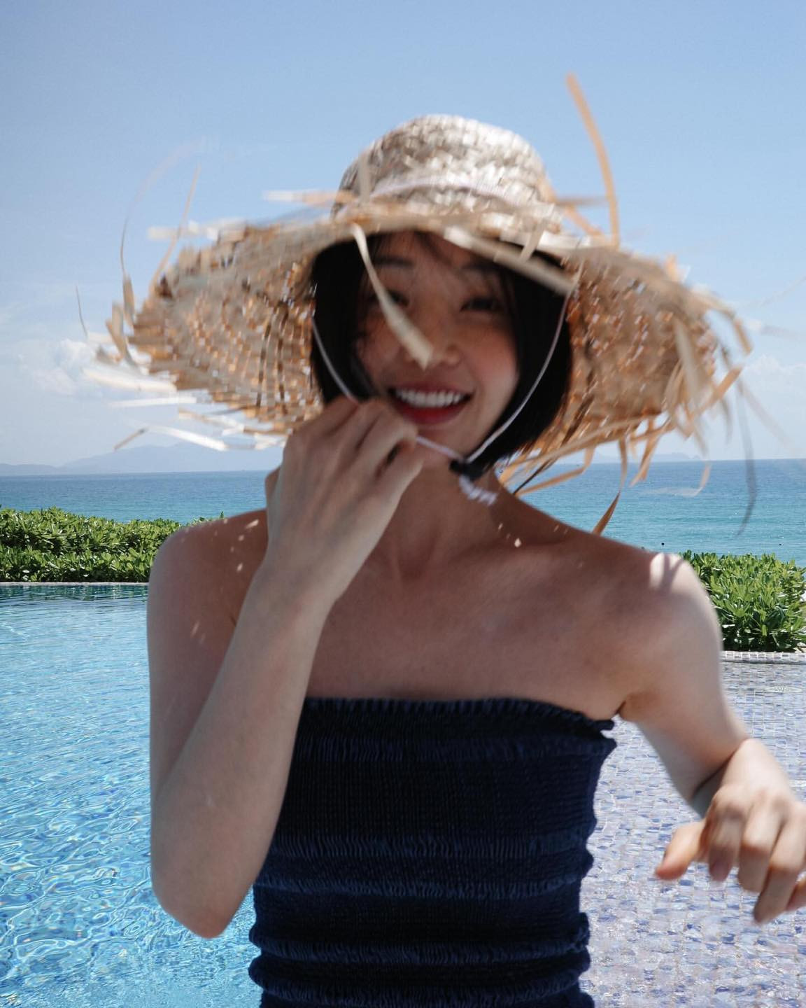 Cô nàng chụp ảnh tại một hồ bơi của resort ngay cạnh bờ biển. Mỹ nhân màn ảnh Hàn diện chiếc áo quây tối màu đơn giản, mang chiếc mũ lá cọ đặc trưng của những khu du lịch biển ở Việt Nam.