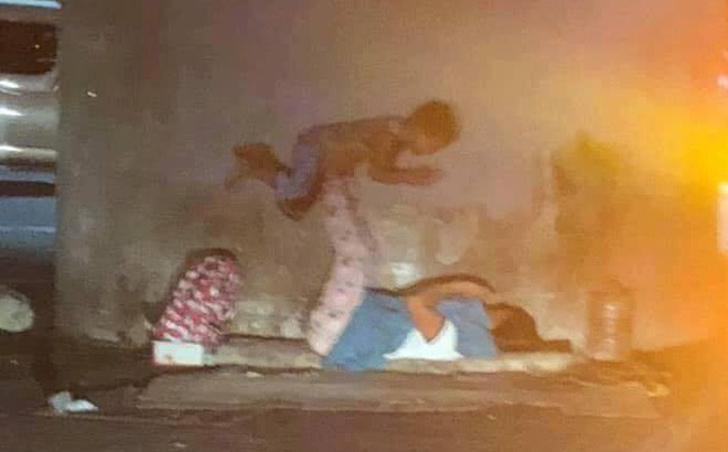 Hình ảnh hai mẹ con chơi trò lái máy bay. Dù đang ở vỉa hè giữa đêm, sống trong hoàn cảnh khó khăn không nhà cửa, người mẹ vẫn cố gắng tìm niềm vui tuổi thơ cho con.