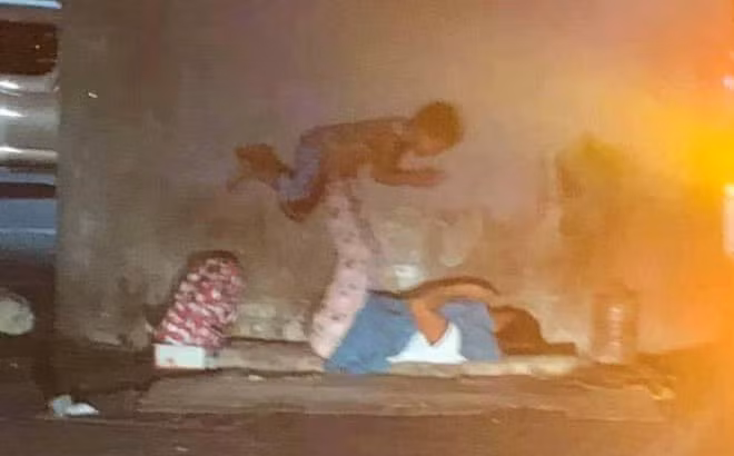 Hình ảnh hai mẹ con chơi trò lái máy bay. Dù đang ở vỉa hè giữa đêm, sống trong hoàn cảnh khó khăn không nhà cửa, người mẹ vẫn cố gắng tìm niềm vui tuổi thơ cho con.