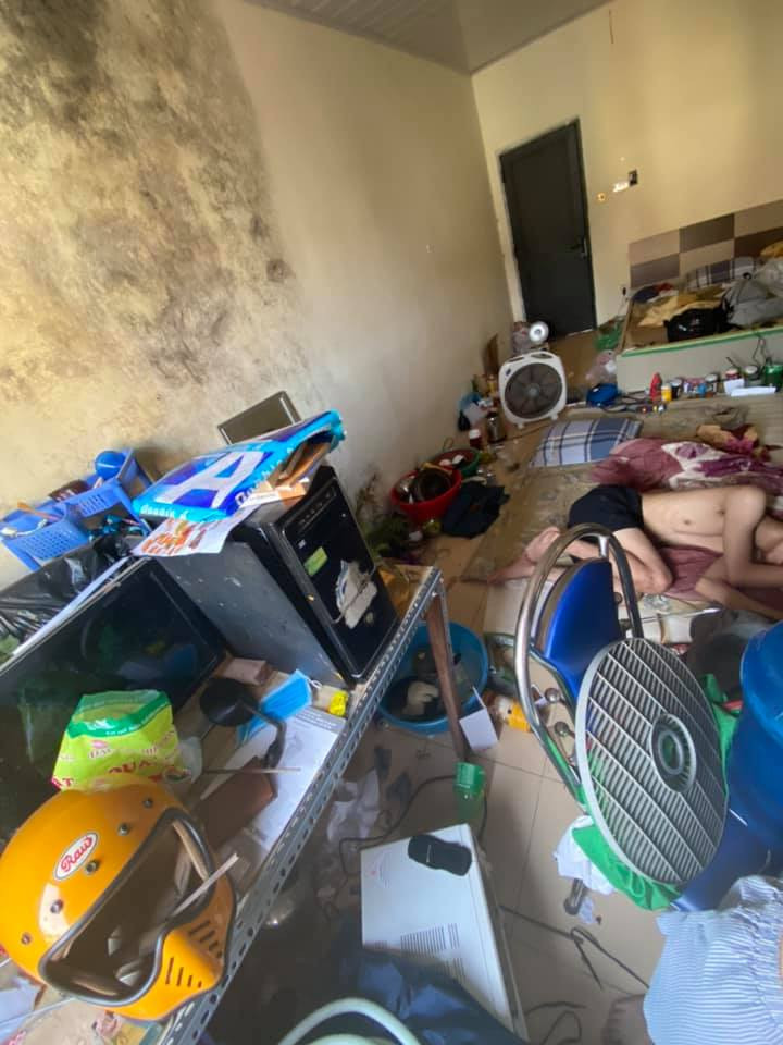 Phần tường trong phòng ẩm mốc, bên dưới là túi rác vứt bừa bãi, lộn xộn lẫn với đồ dùng hàng ngày.