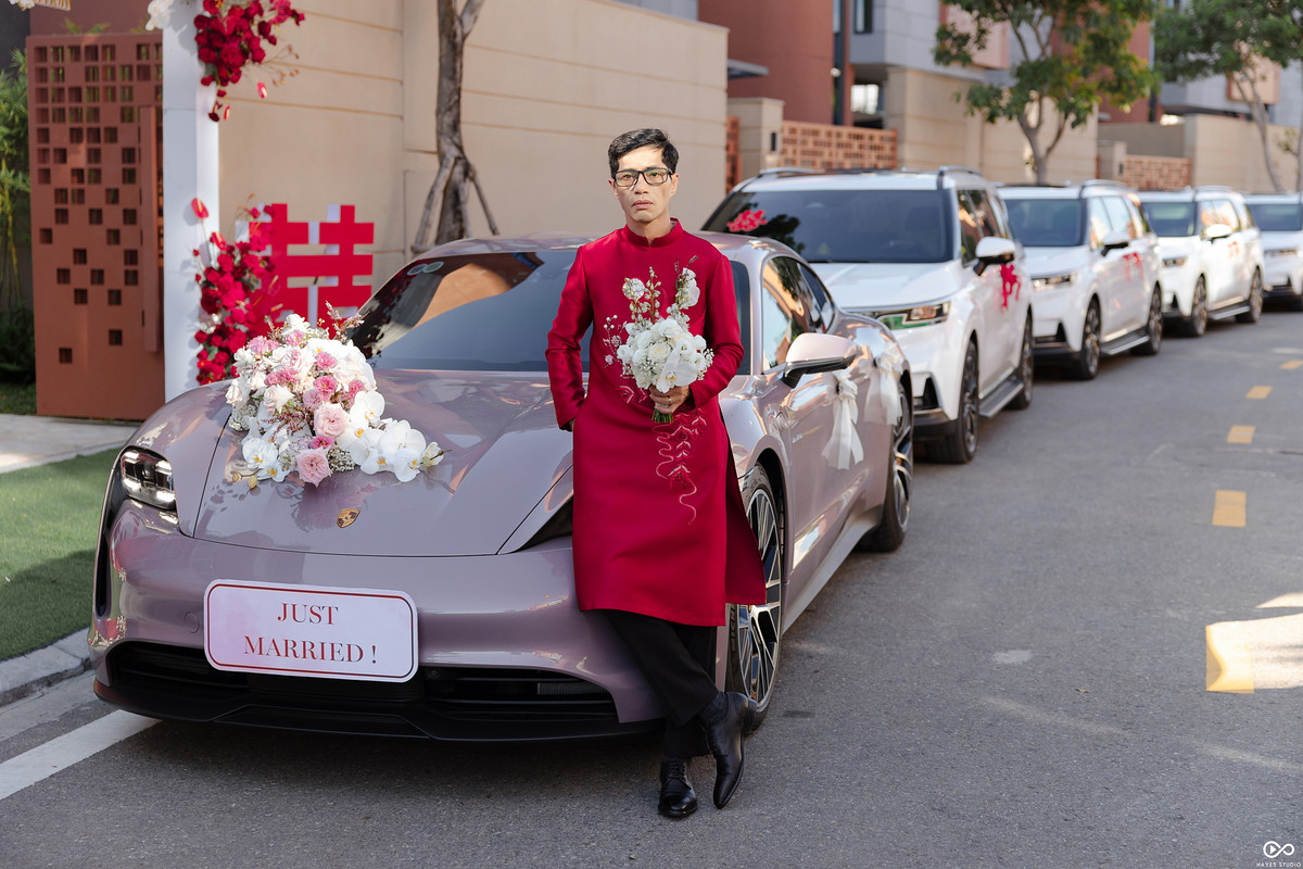 Chú rể trong trang phục áo dài đỏ đứng trước dàn xe nhà trai.