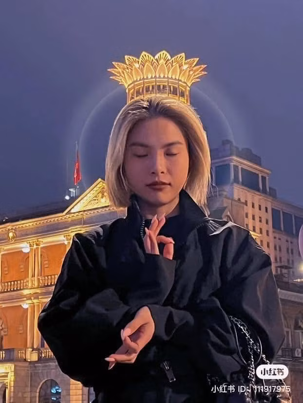 Vào ban đêm, khi những tòa nhà, bến cảng sầm uất lên đèn, Thượng Hải hiện lên như một bức tranh sắc màu rực rỡ. Vậy nên các bạn trẻ đã nghĩ ra góc chụp khiến những chiếc đèn đường, những đỉnh tòa nhà làm nền cho bức ảnh của mình. Trong bức ảnh, cô gái cảm giác như đang đội mão hoa trên đầu, làm nhiều người liên tưởng đến quan thế âm.