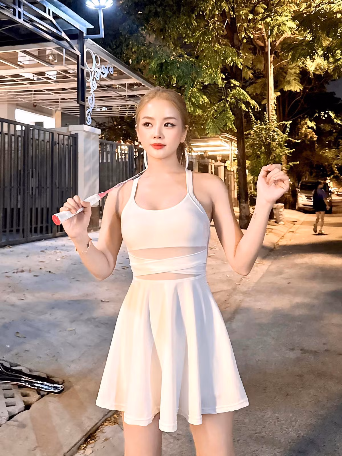 Nàng "búp bê DJ" diện trang phục màu trắng, với phần chân váy xòe và áo ôm sát, tạo dáng bên cây vợt cầu lông màu hồng bánh bèo. Dù trang phục thể thao nhưng Mie vẫn khéo khoe được body hút mắt.