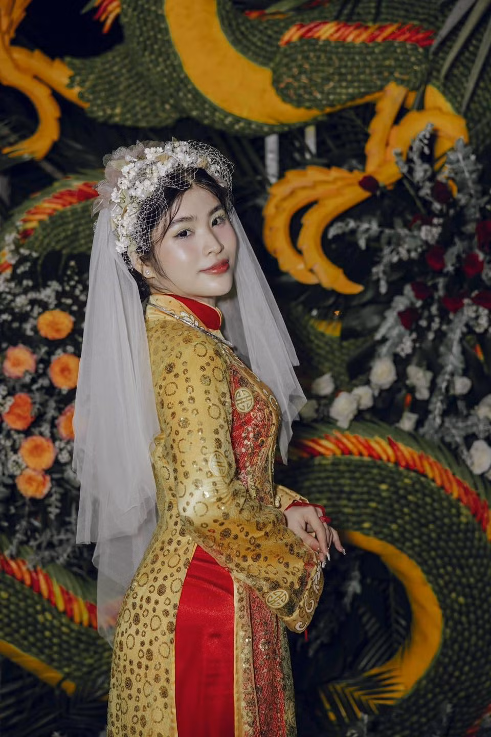 Trong đám cưới này, cô dâu diện áo dài đỏ có họa tiết màu vàng phối cùng áo choàng ren, đội voan trắng, đeo kiềng vàng trên cổ. Chú rể mặc bộ vest màu xám bạc với chất vải bóng phối cùng cà vạt sọc đỏ.