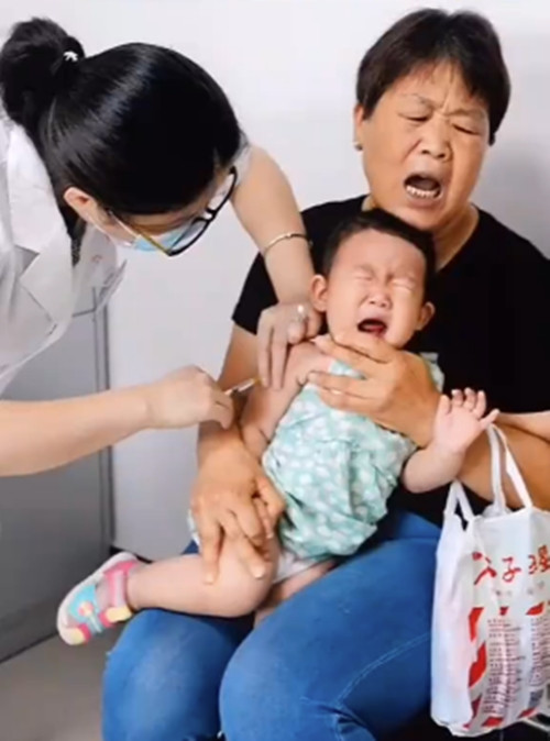 Khi mũi tiêm được đâm vào, bây giờ cảm nhận được nỗi đau nên em bé òa khóc, biểu cảm của người bà bên cạnh cũng mếu máo không kém.