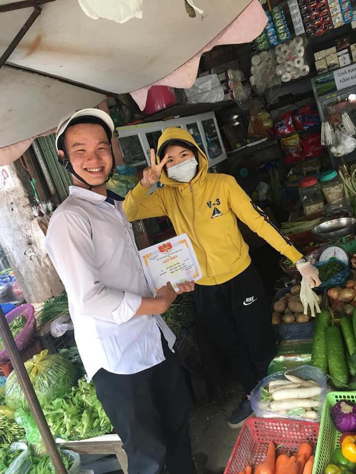 Chị bán hàng rau củ cũng cảm thấy vui vẻ khi Hiếu cầm tờ giấy khen, thể hiện ở cách tạo dáng của chị khi chụp.