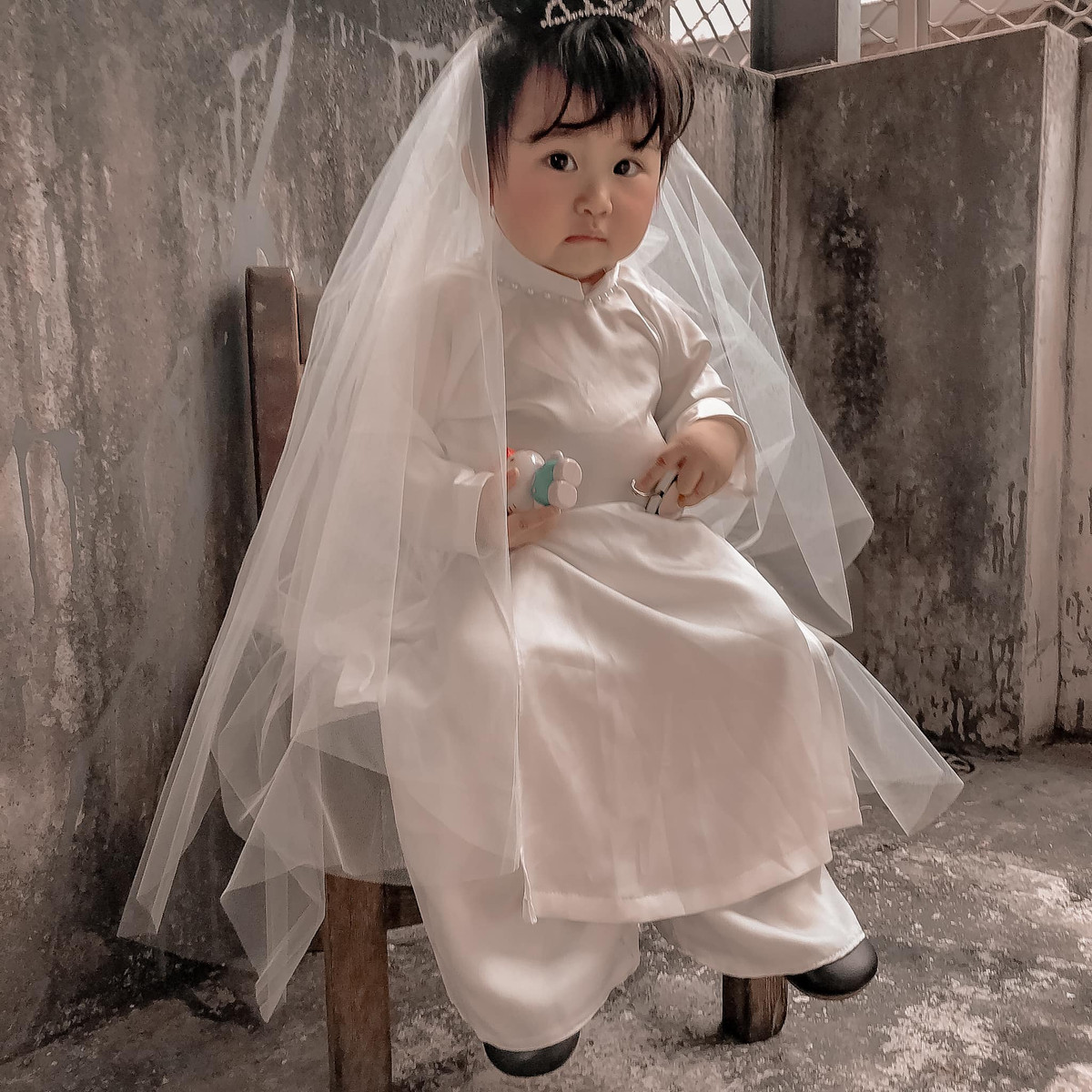 Để ý kỹ mới thấy, phần mái tóc của "cô dâu" hoàn toàn là giả vô cùng buồn cười. Trẻ con hiếu động nên không tránh khỏi mái tóc xô lệch trong lúc chụp ảnh.