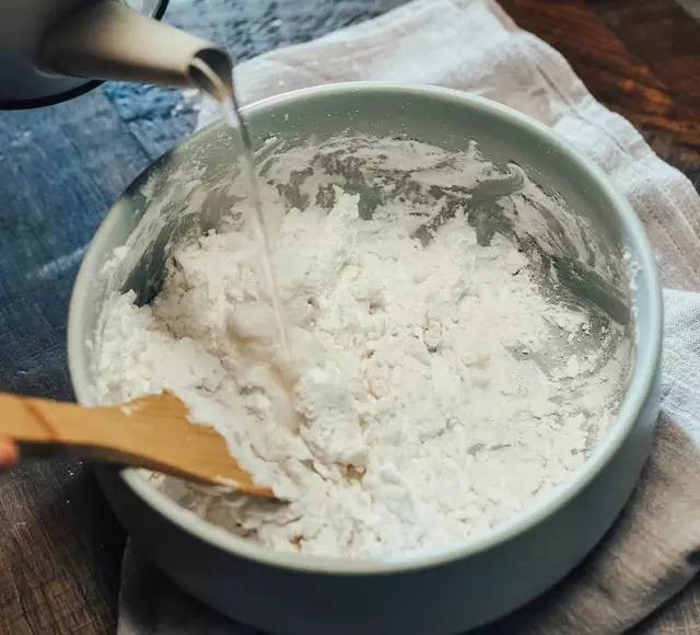 Để làm được món bánh trôi pha lê xinh đẹp này, bước 1 chị em mình đổ bột năng vào một cái bát to, từ từ đổ nước sôi vào và khuấy đều cho đến khi hỗn hợp mịn màng, không còn thấy bột khô. Lưu ý, lượng nước cần thiết cho 100g bột năng là khoảng 90ml.