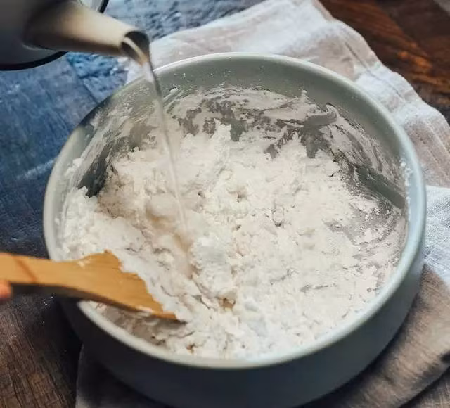 Để làm được món bánh trôi pha lê xinh đẹp này, bước 1 chị em mình đổ bột năng vào một cái bát to, từ từ đổ nước sôi vào và khuấy đều cho đến khi hỗn hợp mịn màng, không còn thấy bột khô. Lưu ý, lượng nước cần thiết cho 100g bột năng là khoảng 90ml.