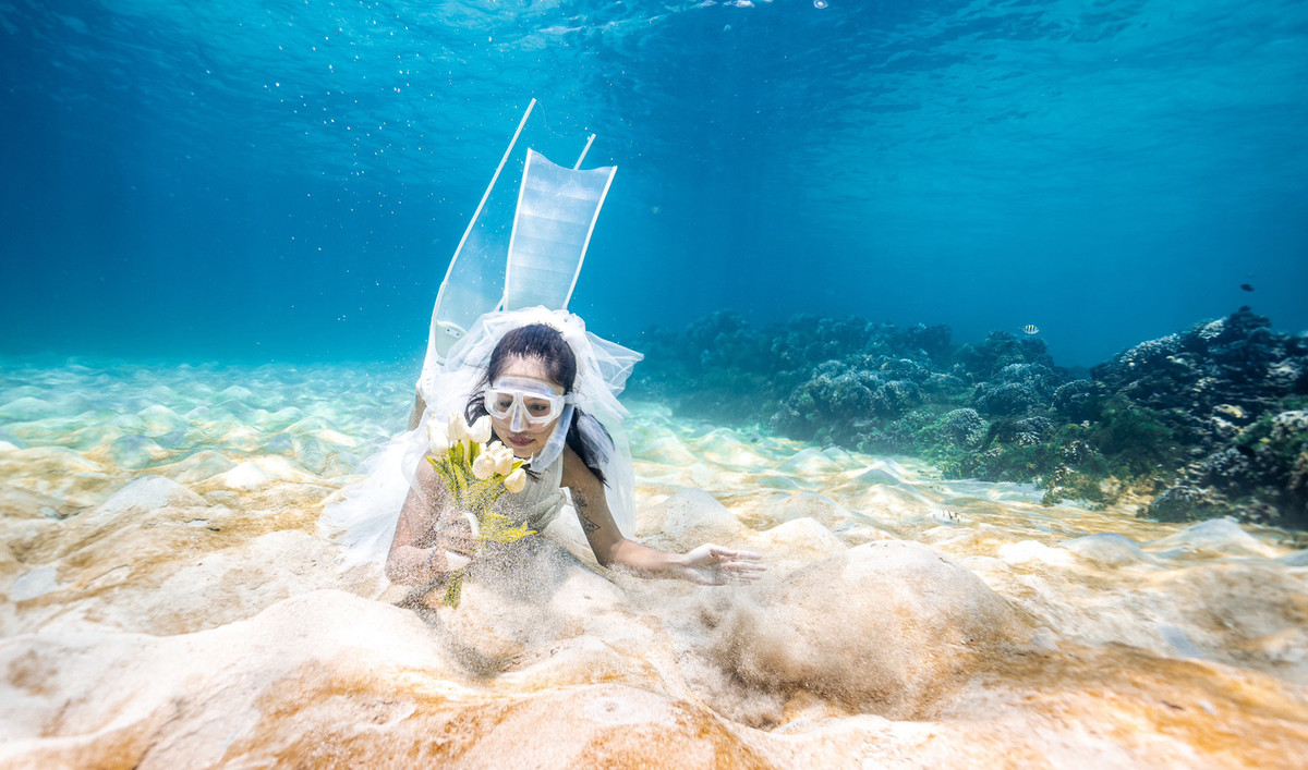 Cô nàng diện váy màu trắng, cầm hoa, tự tin tạo dáng dưới biển.